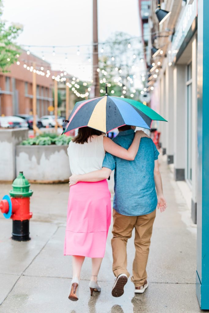 Engaged couple walking under an umbrella together down the sidewalk 